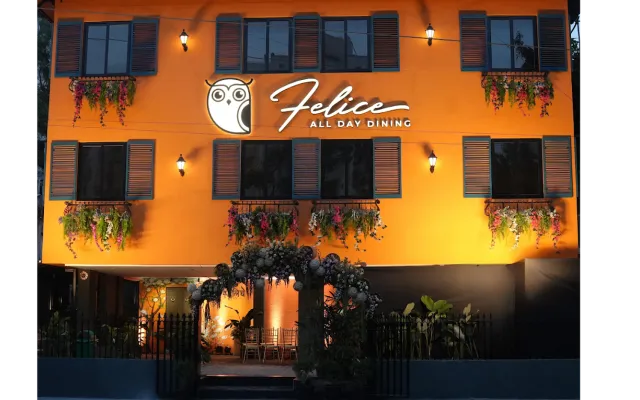The orange facade of Felice All Day Dining at dusk, with its owl sign lit